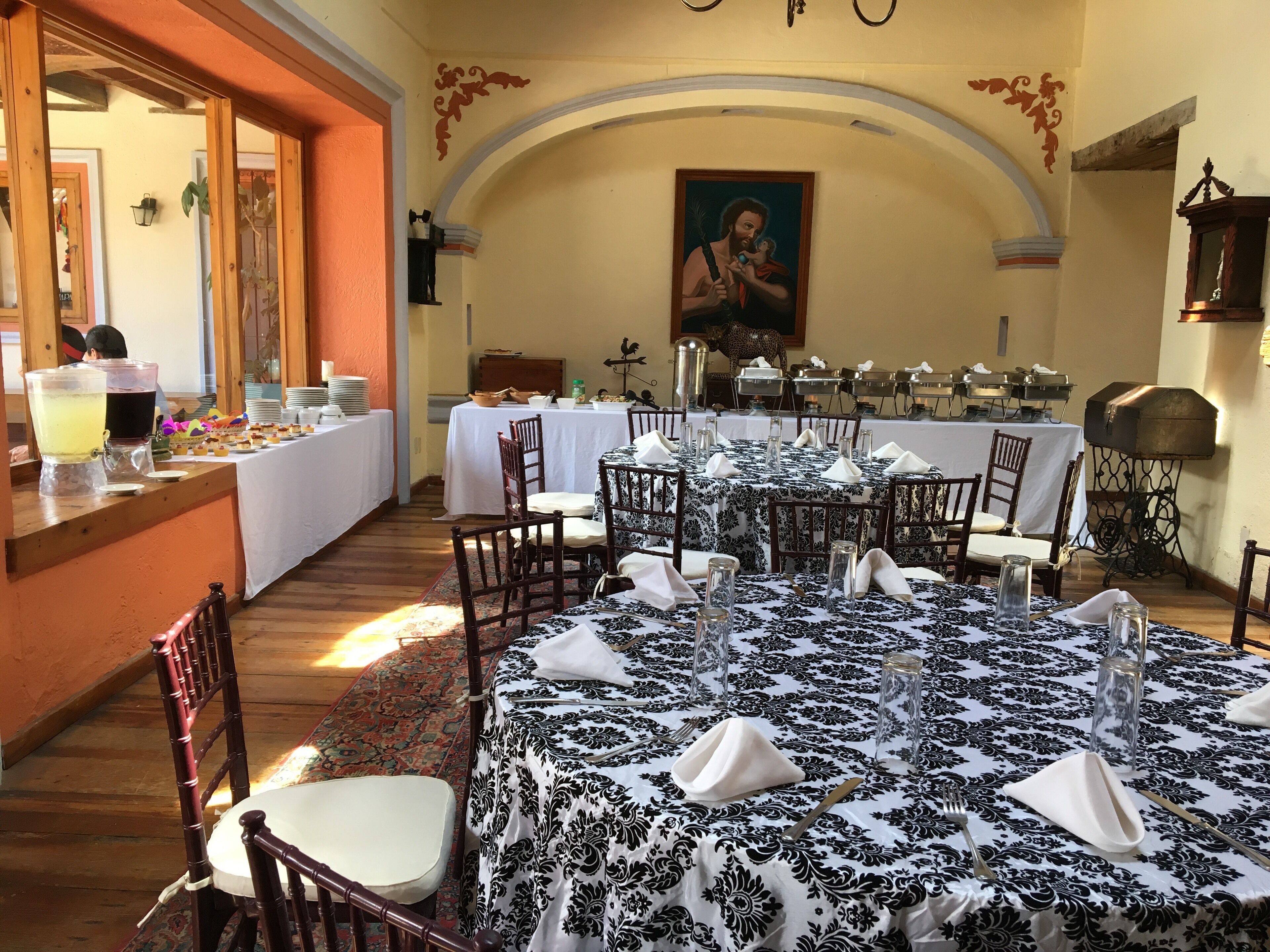 A dining area with round tables set for a meal, featuring black and white tablecloths, white napkins, and clear glassware.