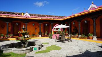 Un patio con una fuente, plantas en macetas, mobiliario exterior y un techo de tejas.