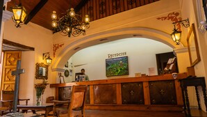 Un área de recepción con un mostrador de madera, una araña de cristal y un cuadro en la pared.