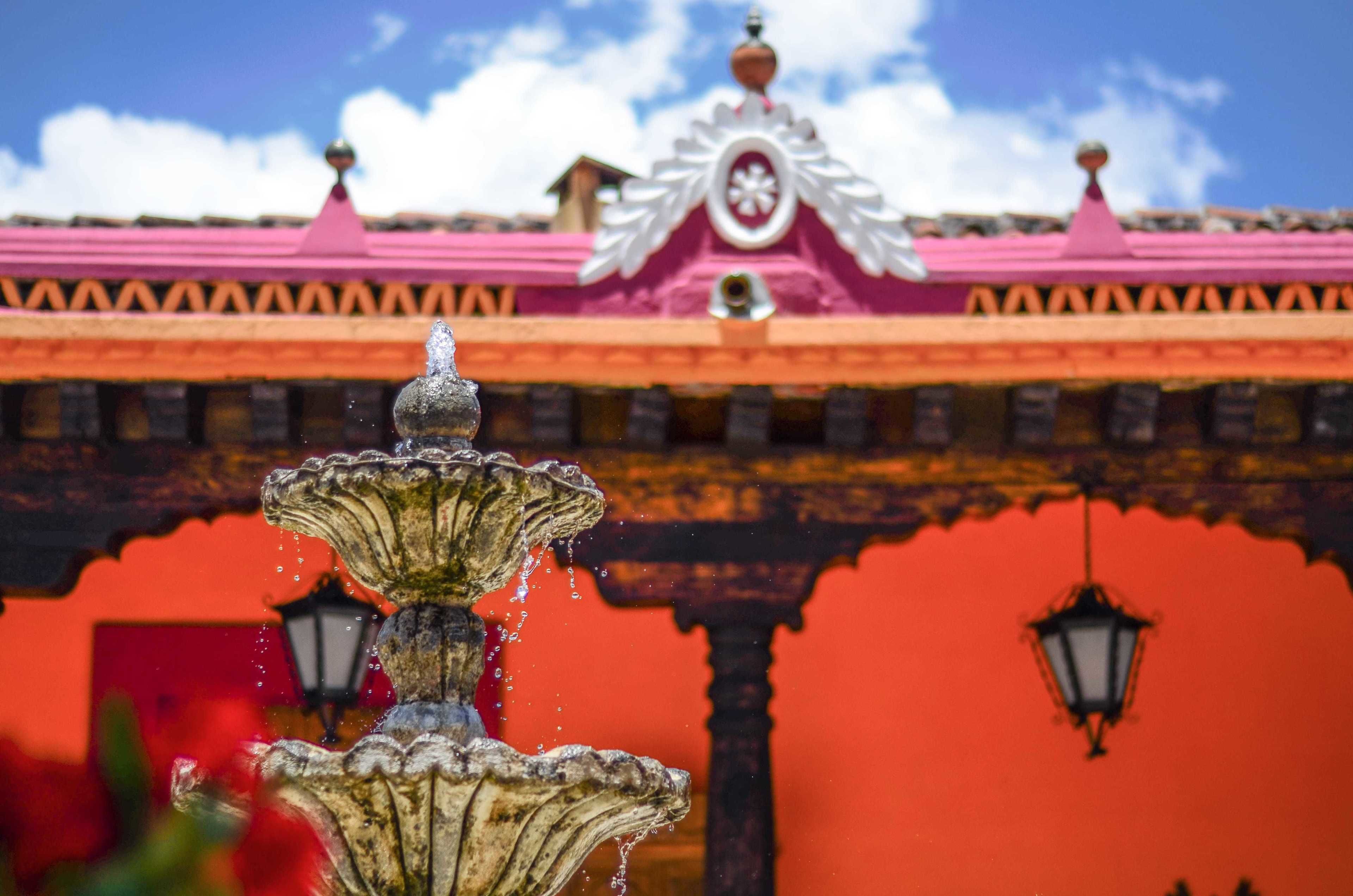 A fountain in the foreground with a building in the background featuring a pink roof and a decorative emblem.