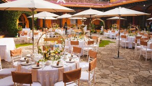 Un patio al aire libre con mesas redondas dispuestas para comer, rodeado de sombrillas blancas y sillas.