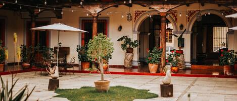 A courtyard with tiled flooring, potted plants, outdoor furniture, and a tiled roof structure.