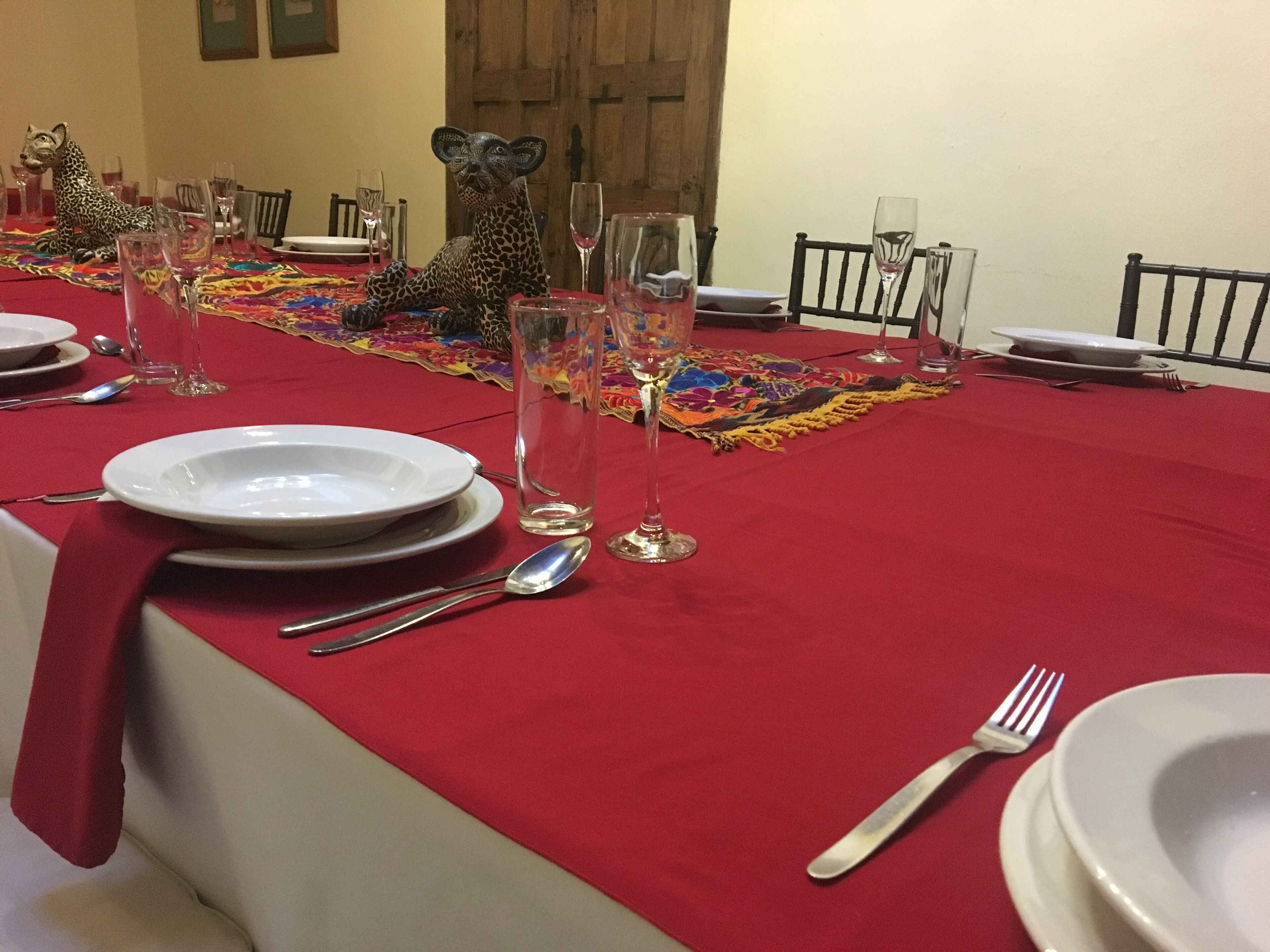 Una mesa de comedor dispuesta con platos, cubiertos y cristalería, cubierta con un mantel rojo.