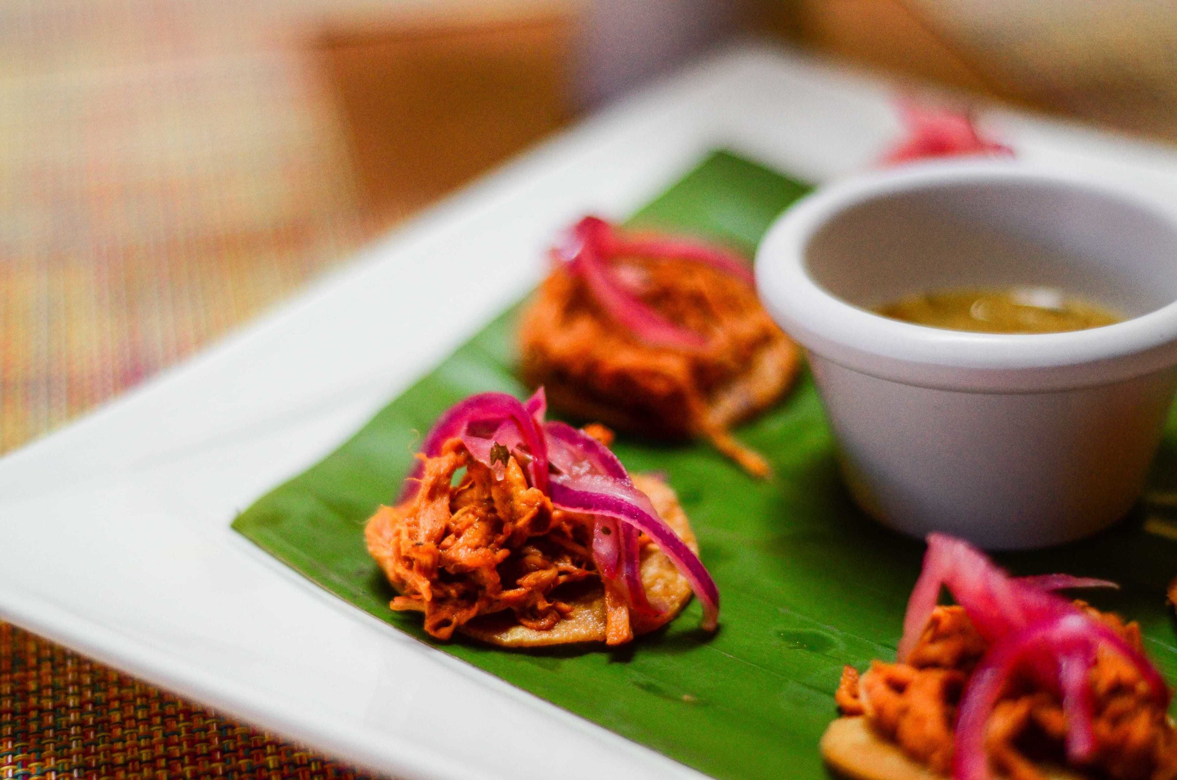 A plate of food with shredded meat and red onions on a banana leaf, accompanied by a small bowl of sauce.