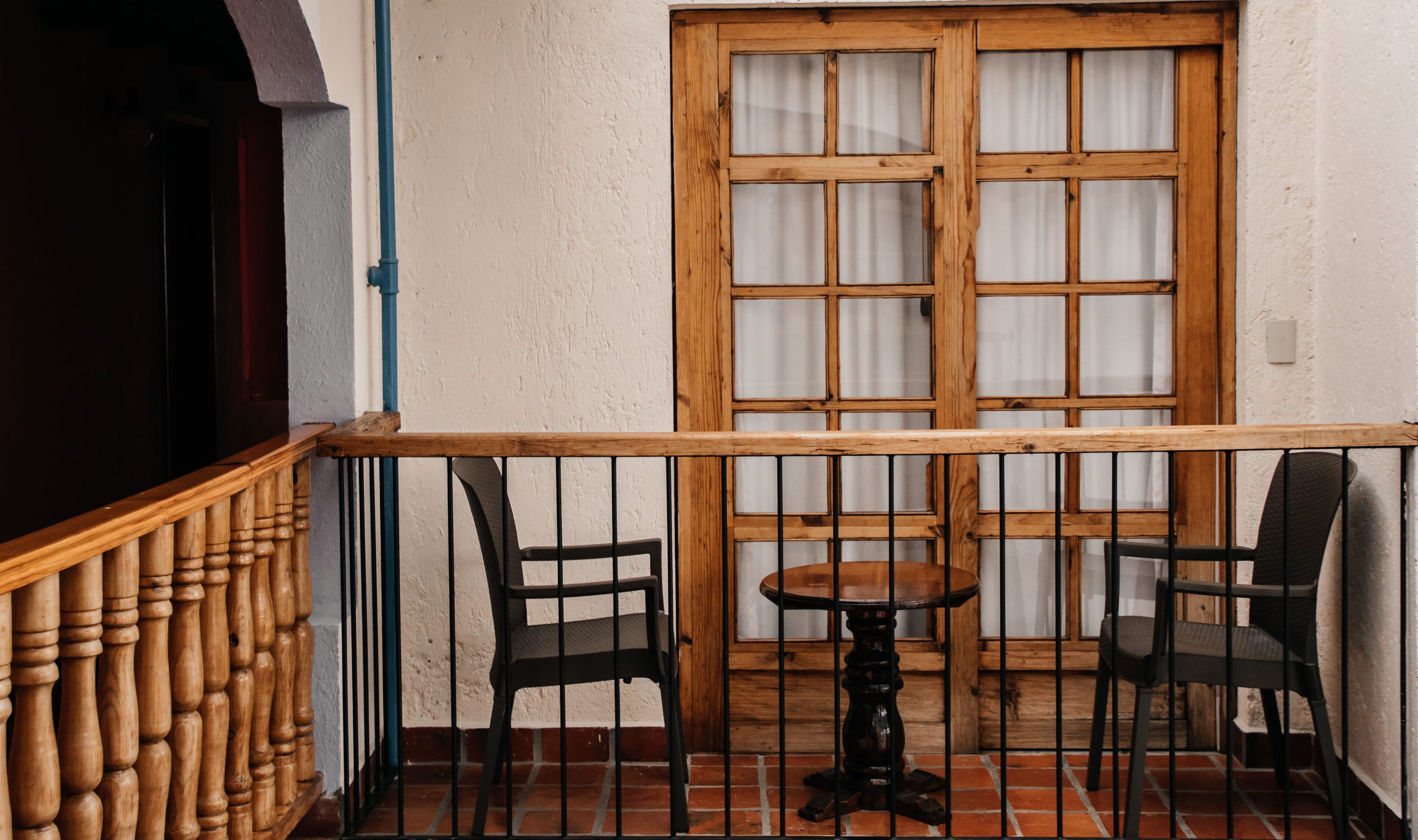 Un balcon doté d’une balustrade en bois, de deux chaises, d’une petite table ronde et d’une fenêtre à carreaux.