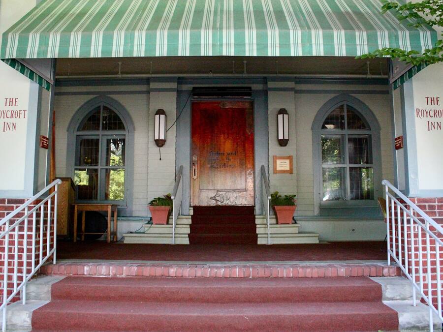 A hotel entrance with a red door, a green and white striped awning, and two potted plants on either side of the steps.