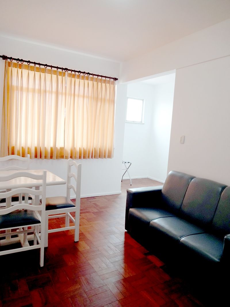 A living room with a black sofa, a white dining table with chairs, and a window with curtains.