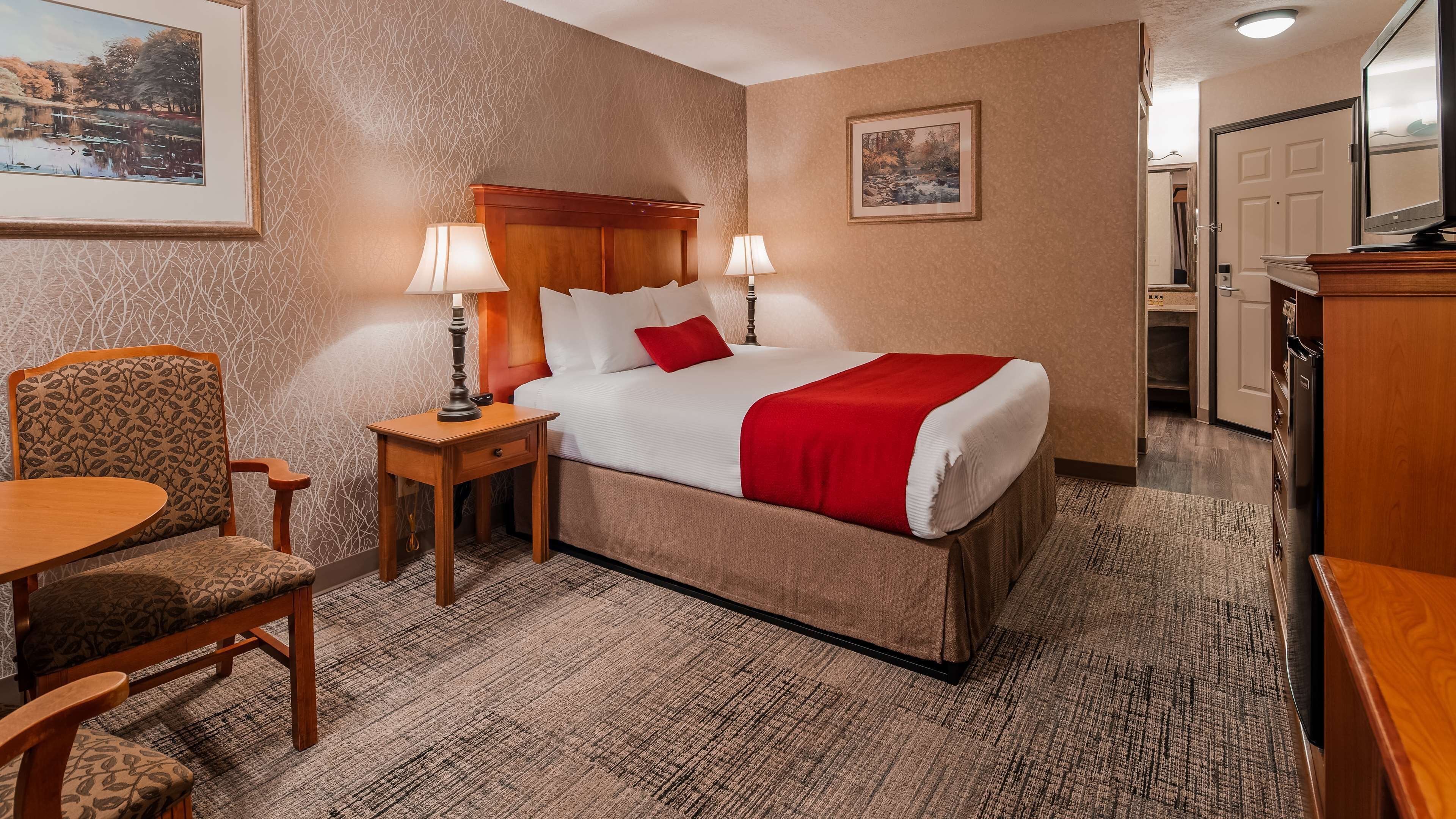 Habitación de hotel con cama, dos lámparas de noche, una silla, una mesita y un televisor.