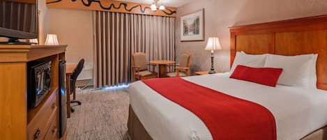 Ein Hotelzimmer mit einem Bett, einem Schreibtisch, einem Stuhl, einem Fernseher und einem Vorhangfenster.