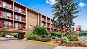 A multi-story hotel with a red and beige facade, a lobby entrance, and a large tree in front. - Best Western Plus Rivershore Hotel (Oregon City)