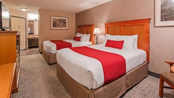 Une chambre d’hôtel avec deux lits, un bureau, une chaise et une salle de bain visible au fond.
