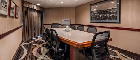 A conference room with a long table, chairs, a projector screen, and framed pictures on the walls.