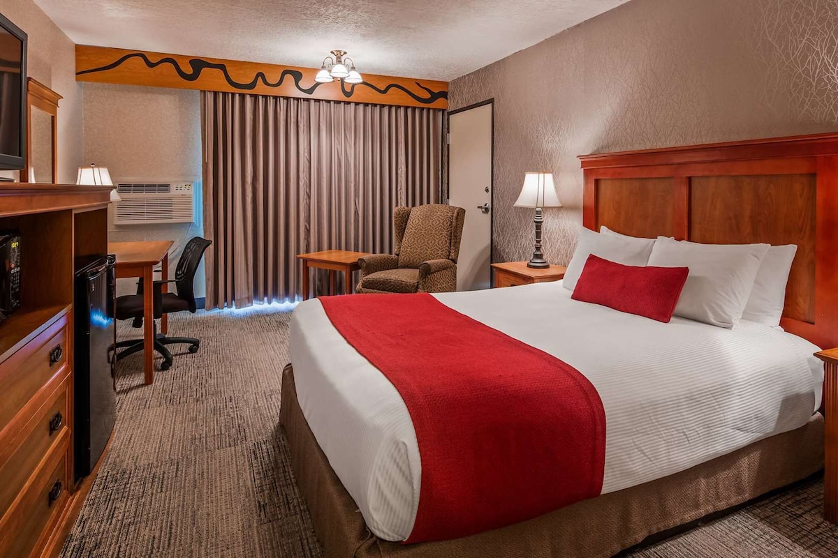 A hotel room with a bed, a desk, a chair, a television, and a lamp.