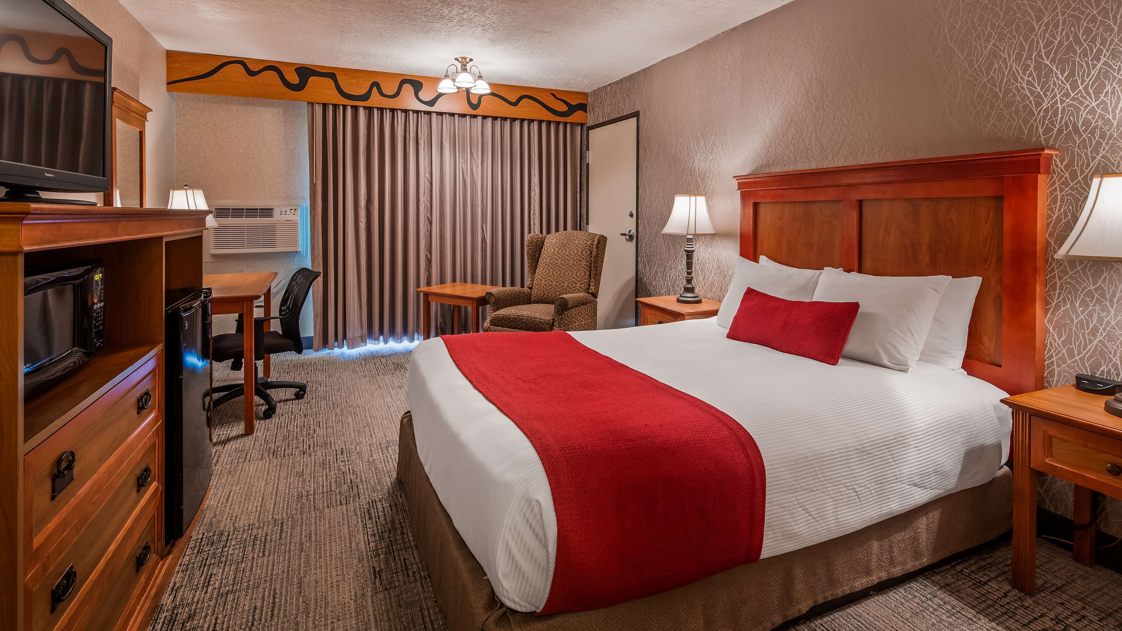 A hotel room with a large bed, a desk with a chair, a television, a microwave, and a wardrobe.