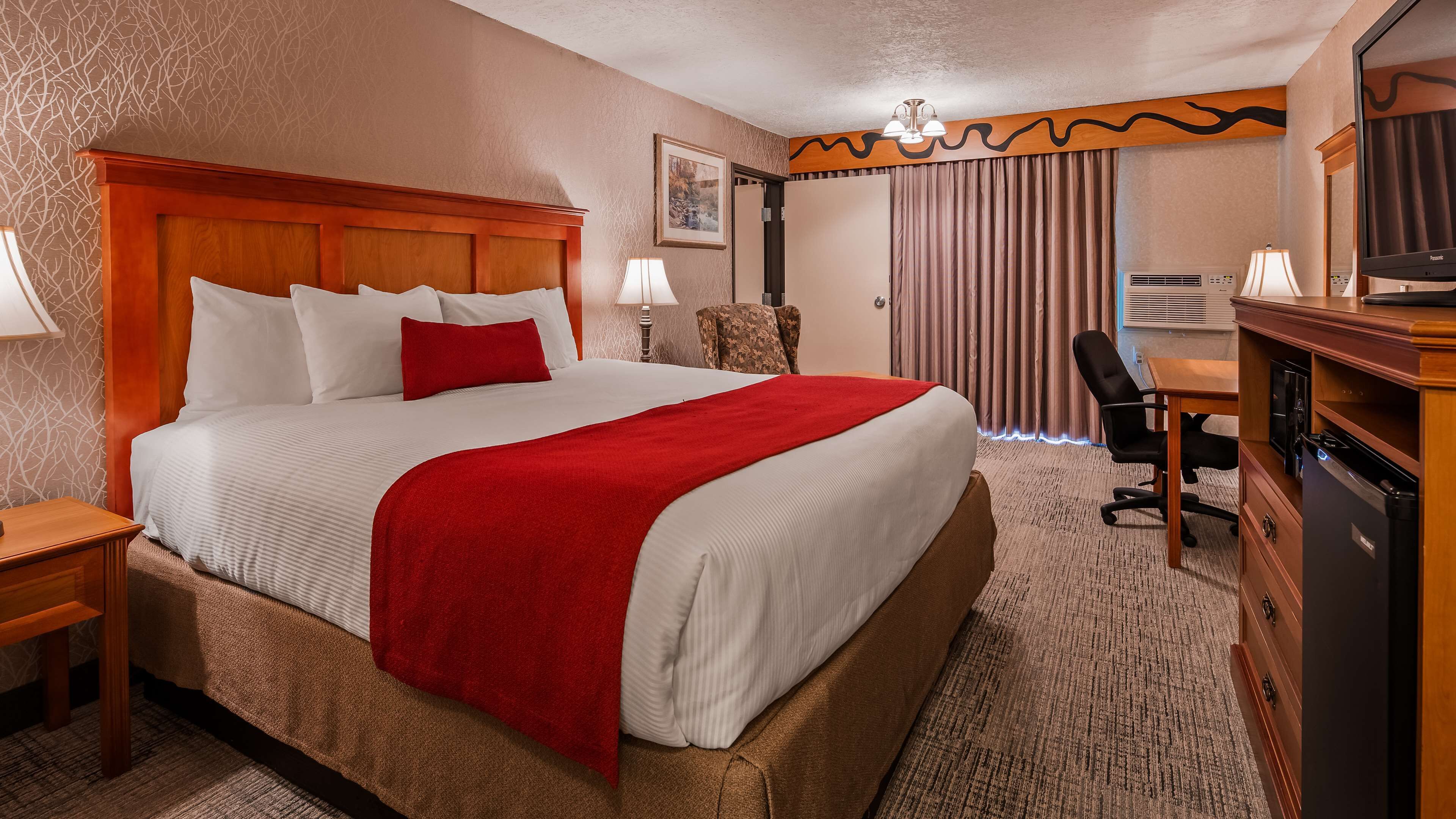 A hotel room with a large bed, a desk, a chair, a television, and a wardrobe.