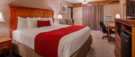 A hotel room with a large bed, a desk, a chair, a television, and a wardrobe.