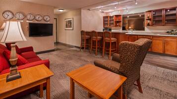 A hotel room with a living area, a kitchen, and a bar area. There are clocks on the wall, a television, and a bar with stools.