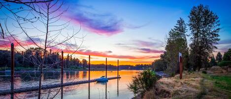A calm lake with a dock and a boat, surrounded by trees and a clear sky.