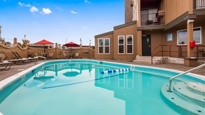 A swimming pool with lounge chairs and umbrellas, a building with a balcony, and a fence.