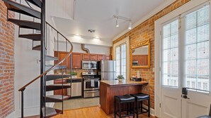 A modern kitchen with a central island, stainless steel appliances, and a brick accent wall. - Grenoble House (New Orleans)