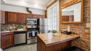 A kitchen with wooden cabinets, stainless steel appliances, a tiled island, and a coffee bar. - Grenoble House (New Orleans)