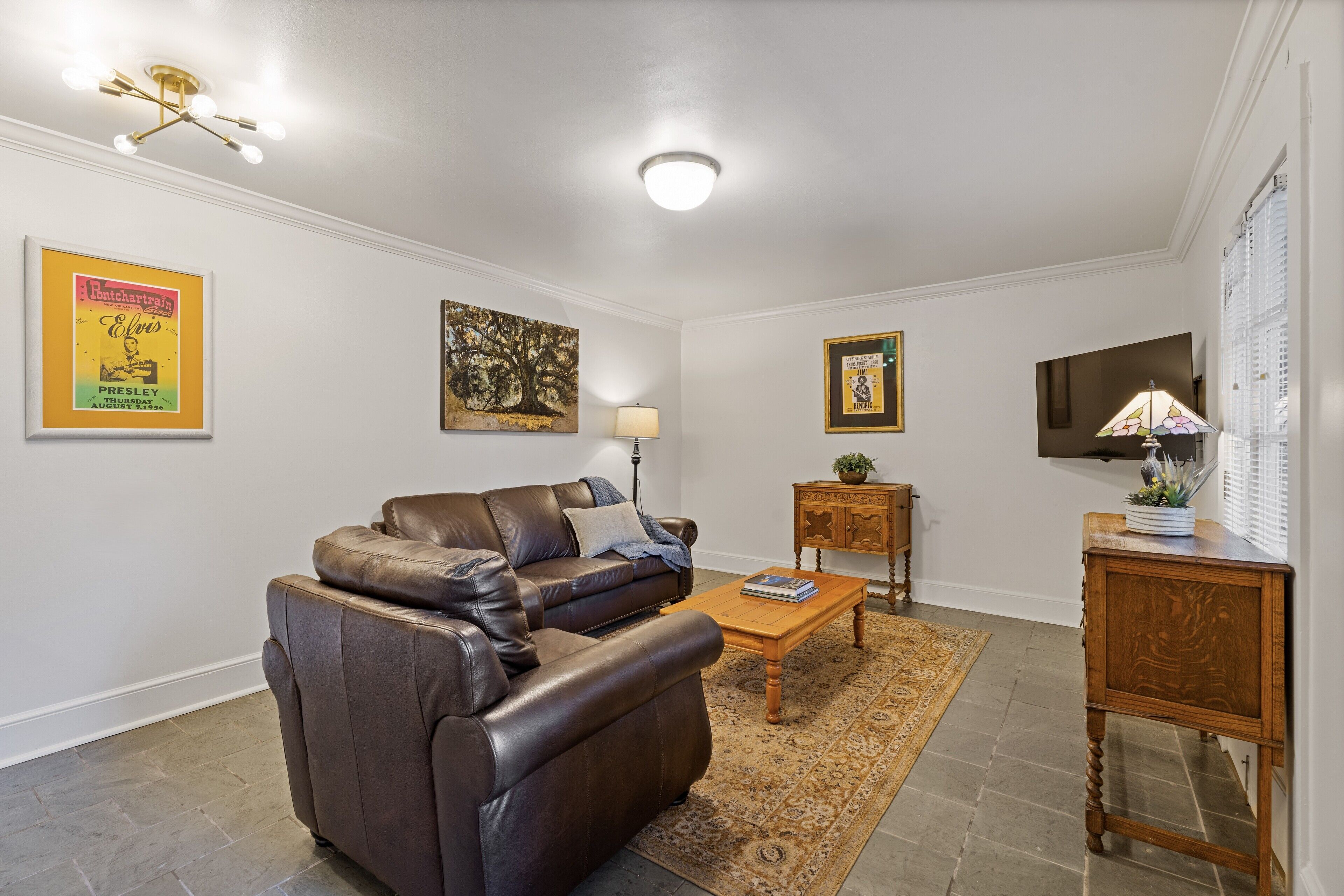 Un salon avec un canapé en cuir marron, une table basse en bois, un tapis à motifs et une petite table d’appoint en bois.