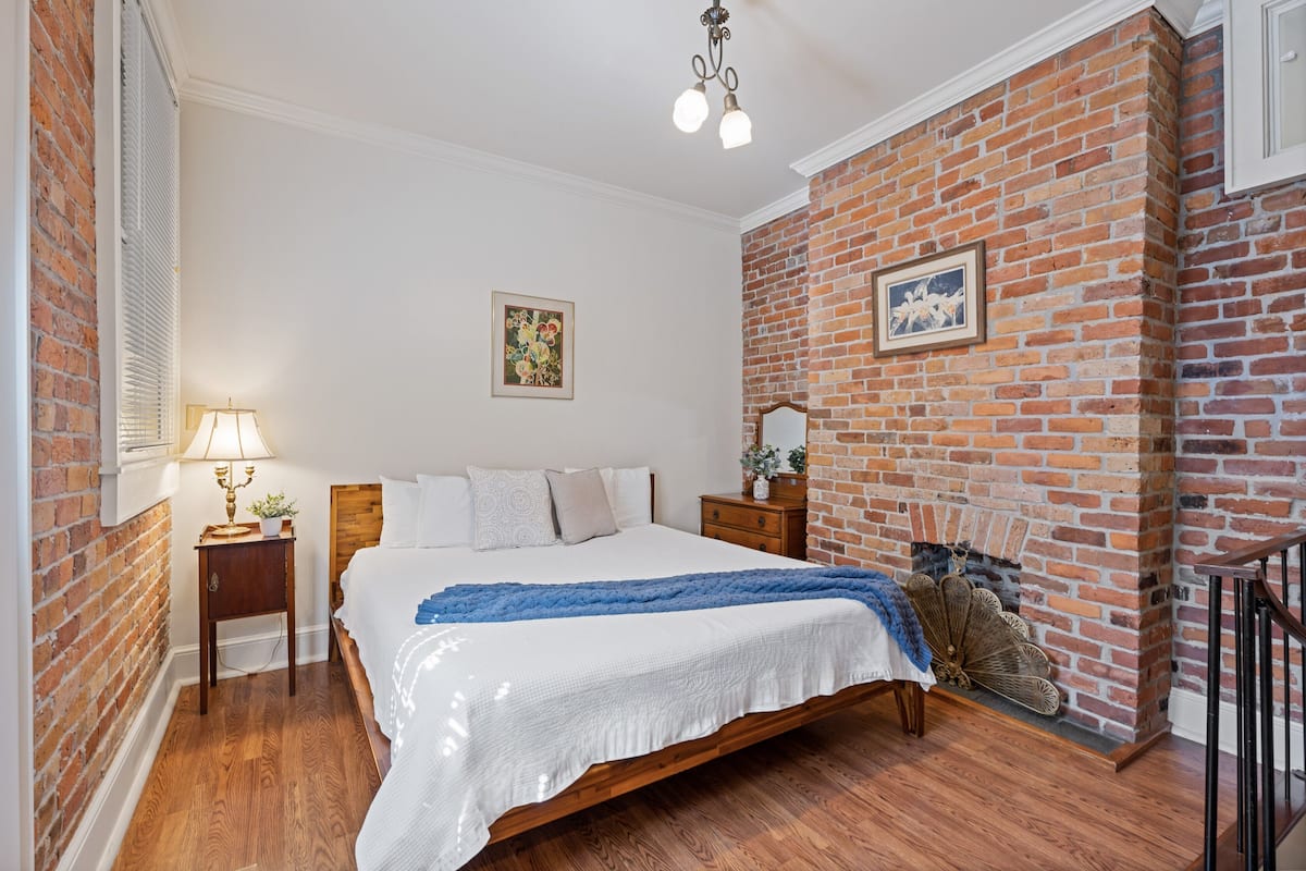 A bedroom with a brick wall, wooden bed, nightstands, and a hanging fan.