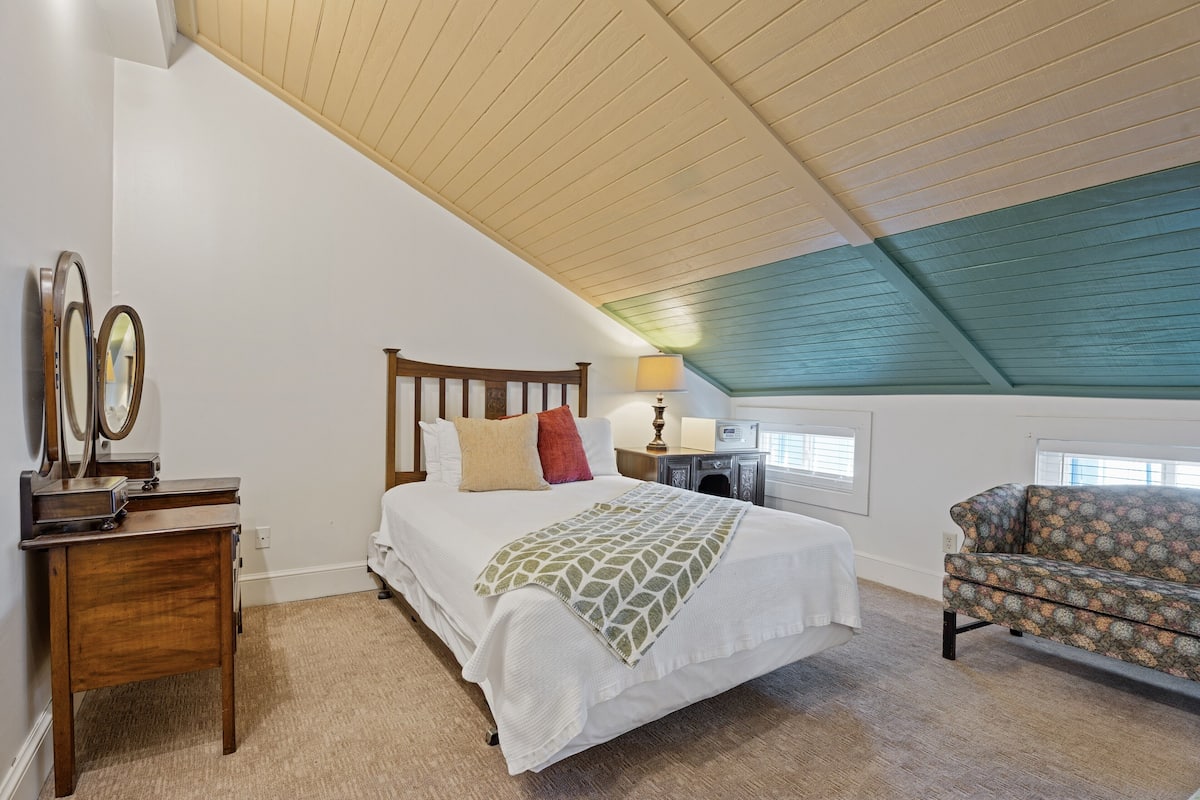 A bedroom with a wooden bed, bedside tables, a chair, and a ceiling with wooden beams.