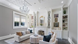 A spacious living room with a fireplace, white furniture, and decorative items. - Grenoble House (New Orleans)