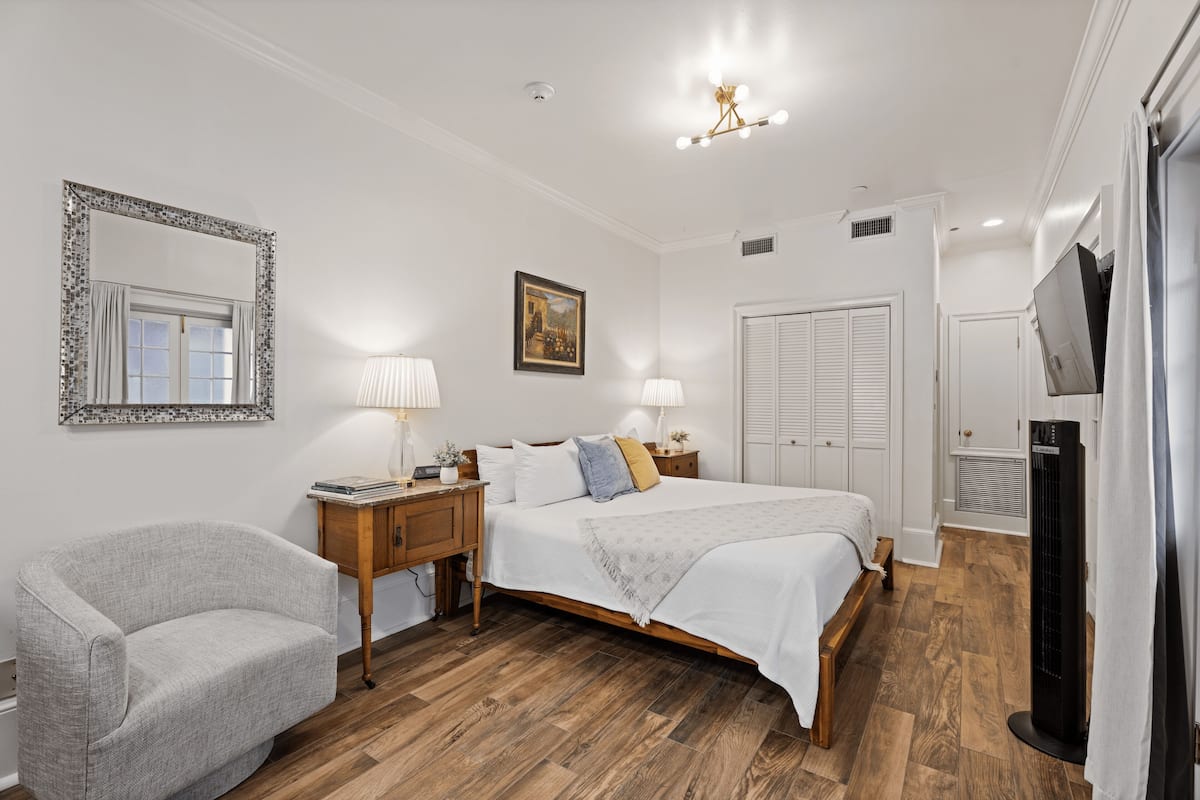A bedroom with a large bed, bedside tables, a chair, a mirror, and a TV.