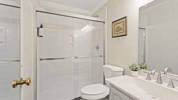 A bathroom with a glass-enclosed shower, a white toilet, a sink with a mirror, and a framed picture on the wall.