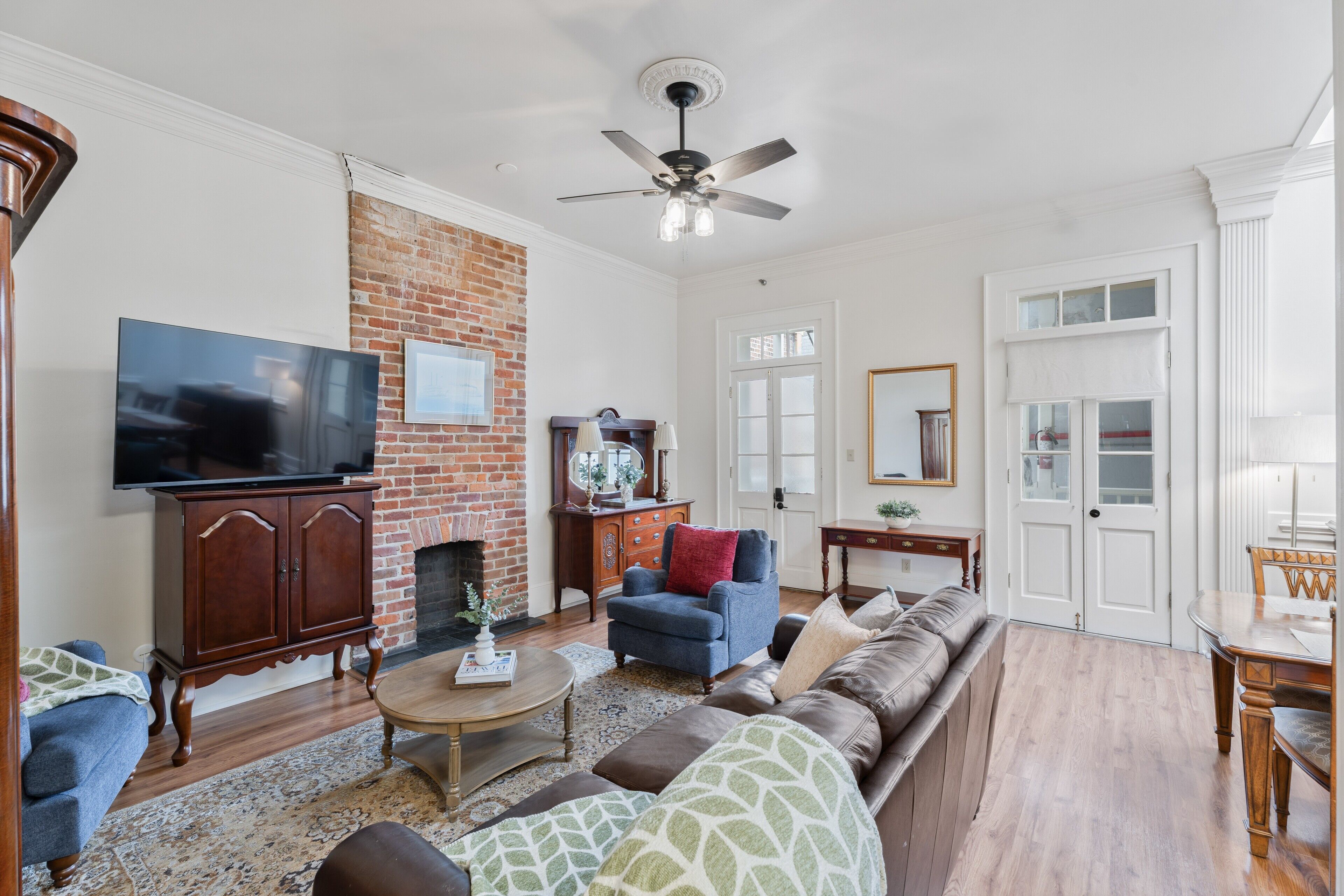 A living room with a brick fireplace, a television, a sofa, and a ceiling fan.