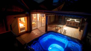 A hot tub area with a wooden deck, a glass door leading to a room with a lit lamp, and a bar area with stools. - Alure Stanthorpe (Mount Tully)
