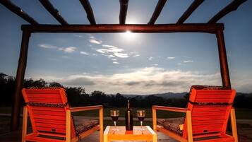 A wooden pergola with two red chairs and a table under a night sky with a visible moon.