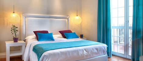 Une chambre moderne avec un grand lit, deux tables de chevet, une plante en pot et une vue par une fenêtre avec des rideaux.