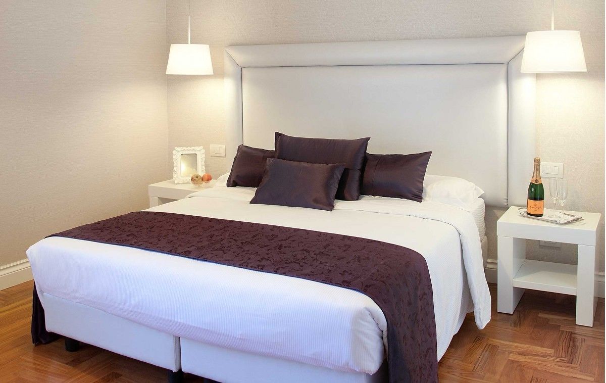 A neatly made bed with a white and dark brown bedspread, two bedside tables with lamps, and a bottle of champagne on one of the tables.