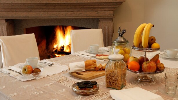 A breakfast setting with a fireplace, bread, fruits, and a jar of jam. - La Villetta Suite (Ciampino)