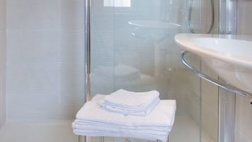 A bathroom with a glass shower enclosure, a white sink, and a stack of folded towels.