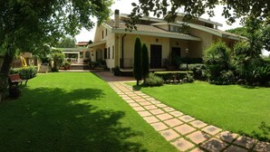 A well-maintained garden with a paved walkway leading to a house with a tiled roof and multiple windows. - La Villetta Suite (Ciampino)