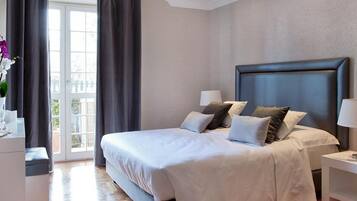 A hotel room with a large bed, two bedside tables, a nightstand, a window with curtains, and a balcony view.