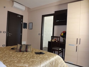 Une chambre d’hôtel comprenant un lit, un bureau avec une chaise, une armoire et un appareil de climatisation.