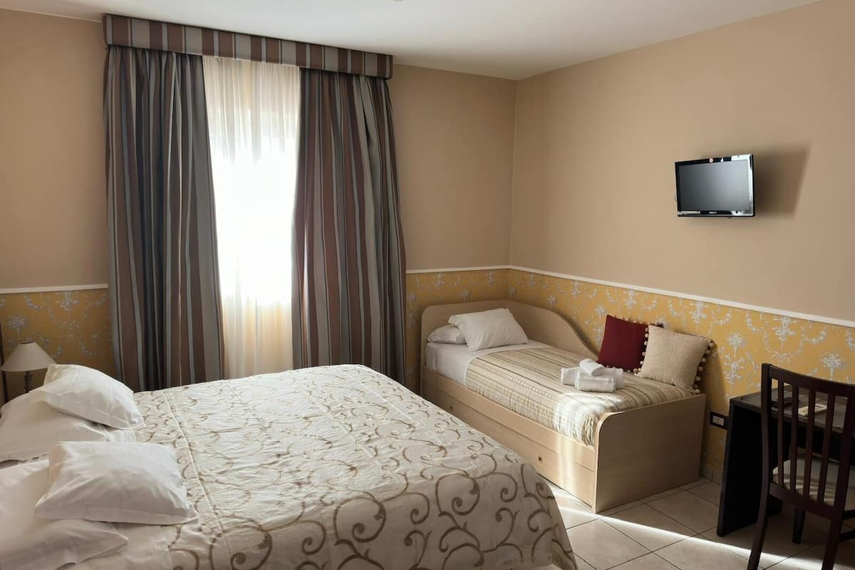 Ein Hotelzimmer mit einem großen Bett, einem kleineren Bett, einem an der Wand befestigten Fernseher und einem Sessel.