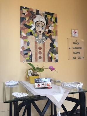 Un mur orné d’une mosaïque, un panneau indiquant l’emplacement des salles, une table avec un menu et une plante en pot.