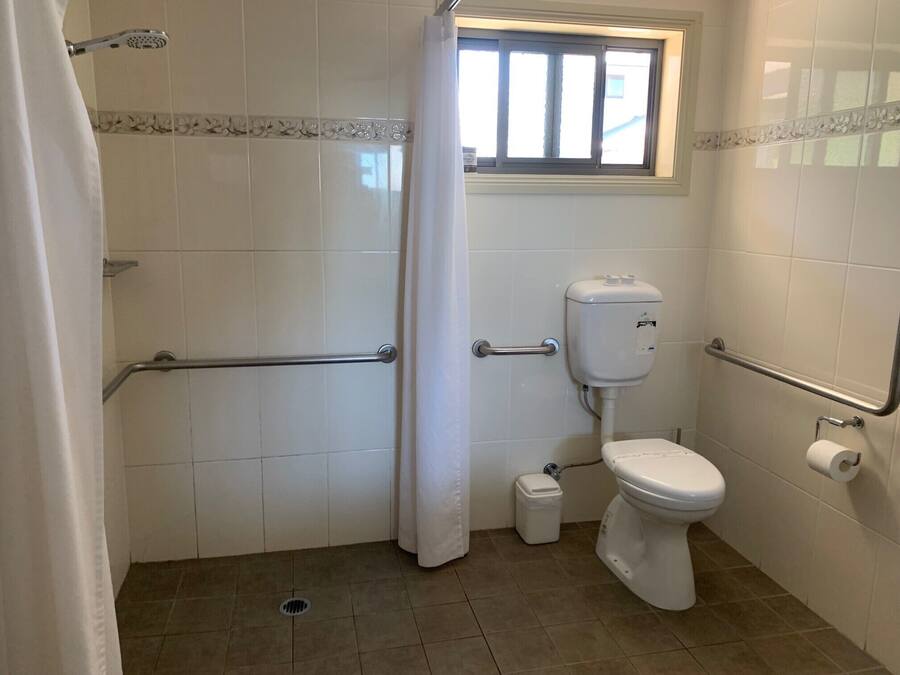 Un baño con ducha, inodoro y barras de apoyo.