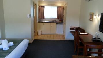 A hotel room with a bed, a desk, a chair, a small kitchenette, and a TV.
