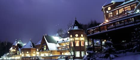 Un grand chalet à étages, doté d’une tour imposante et de nombreux balcons, entouré de neige.