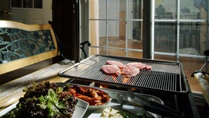 A dining area with a grill, a bench, and a table with food and drinks.