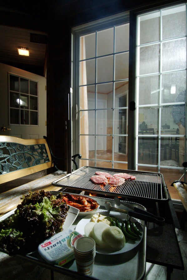 Un comedor con una parrilla, una banca y una mesa con comida y bebidas.