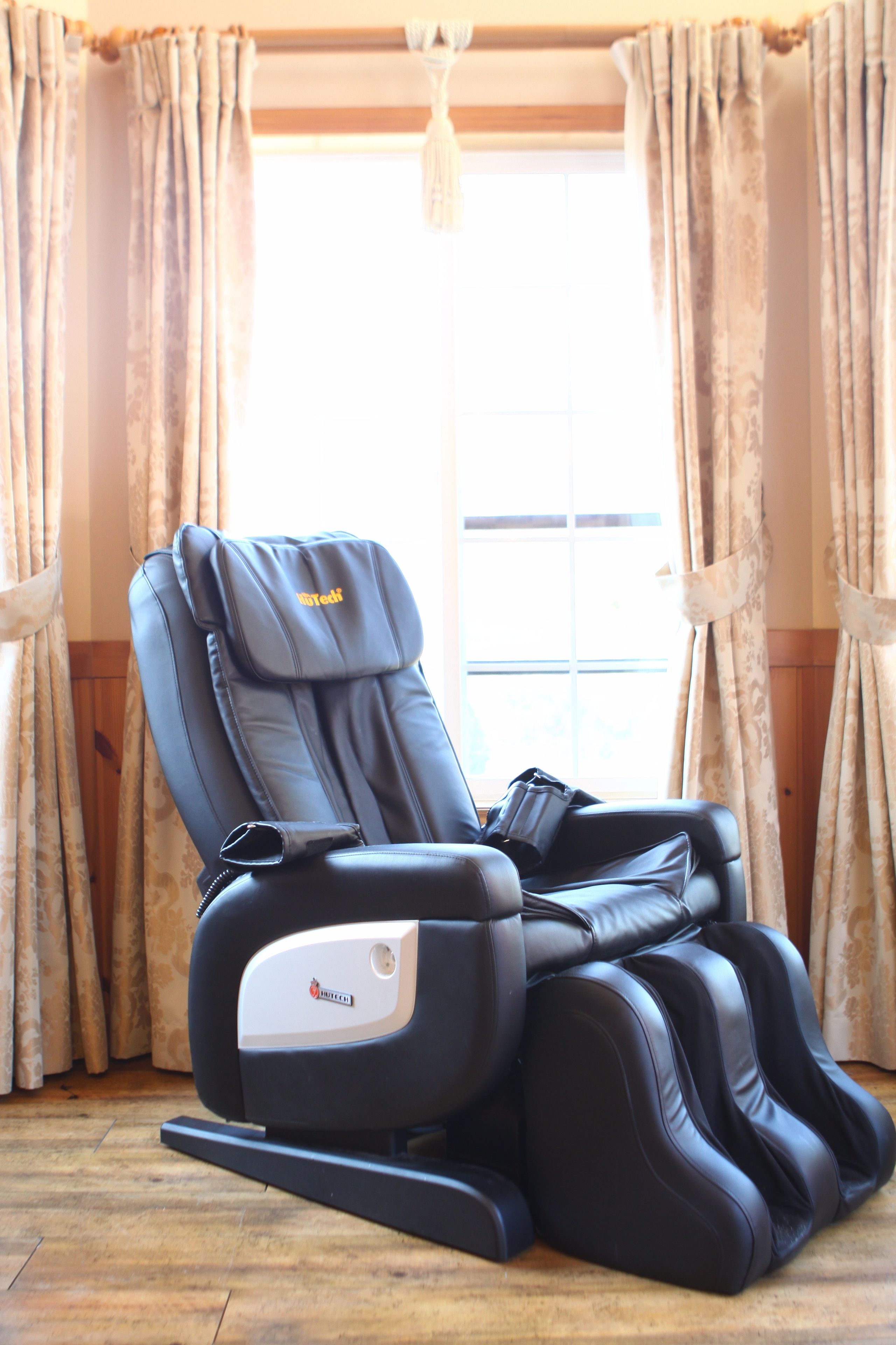 A massage chair in a room with wooden flooring and curtains.