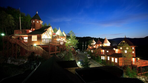 A wooden lodge with multiple buildings, a prominent tower, and a well-lit exterior.